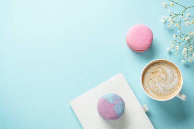 Bir fincan kahve, badem kurabiyesi ve mavi arka planda çiçek. Kopyalama alanı olan üst görünüm.