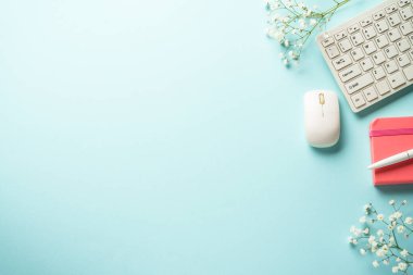 Mavi arka planda klavyesi, defteri, faresi, kalemi ve çiçeği olan ofis işyeri. Kopyalama alanı olan üst görünüm.