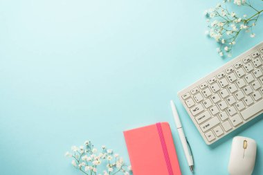 Klavyeli, defterli, mavi arka planda kalem ve çiçekli bir işyeri. Kopyalama alanı olan üst görünüm.