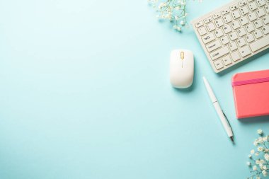 Klavyeli, defterli, mavi arka planda kalem ve çiçekli bir işyeri. Kopyalama alanı olan üst görünüm.