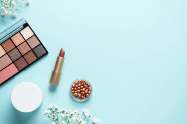 Makyaj paleti, fırçalar ve mavi arka planda ruj. Tasarım için alanı olan üst görünüm.