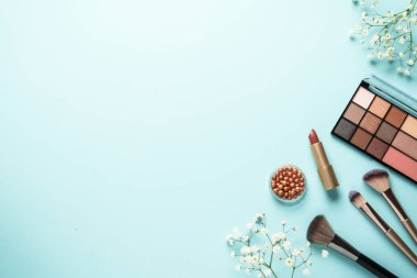 Mavi üzerine düz bir zemin oluşturun. Makyaj paleti, fırçalar ve rahat çiçekli rujlar..