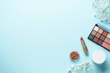 Makyaj ürünleri mavinin üzerine seriliydi. Kozmetik palet, fırçalar, rujlar ve beyaz çiçekler..