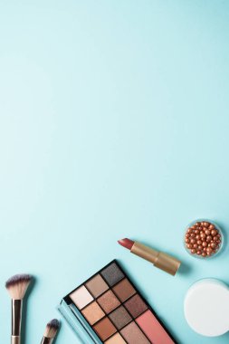 Makyaj ürünleri mavinin üzerine seriliydi. Kozmetik palet, fırçalar, rujlar.