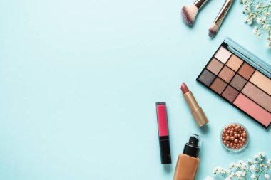 Makyaj ürünleri mavinin üzerine seriliydi. Kozmetik palet, fırçalar, rujlar ve beyaz çiçekler..