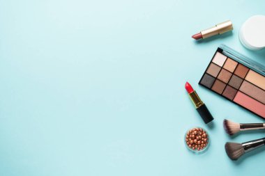 Makyaj ürünleri mavinin üzerine seriliydi. Kozmetik palet, fırçalar, rujlar.