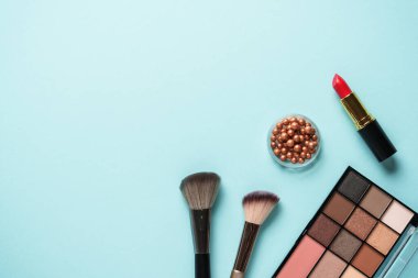 Makyaj paleti, fırçalar ve mavi arka planda ruj. Tasarım için alanı olan üst görünüm.