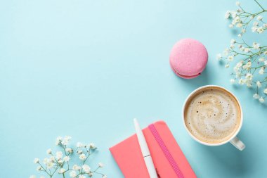 Bir fincan kahve, badem kurabiyesi ve mavi arka planda çiçek. Kopyalama alanı olan üst görünüm.