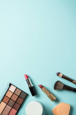 Mavi arka plandaki ürünleri uydur. Kozmetik palet, fırça, krema kavanozu ve ruj. Kopyalama alanı olan düz, dikey.