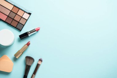 Mavi arka plandaki ürünleri uydur. Kozmetik palet, fırça, krema kavanozu ve ruj. Kopyalama alanı olan düz.