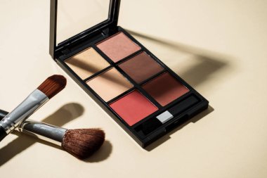 Pastel arka planda sert gölgeli palet ve kozmetik fırçalar yap.