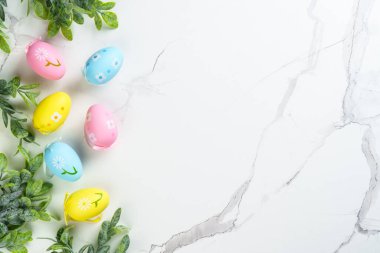 Beyaz arka planda renkli yumurtalar ve yeşil bitkilerle Paskalya kompozisyonu. Kopyalama alanı olan düz.