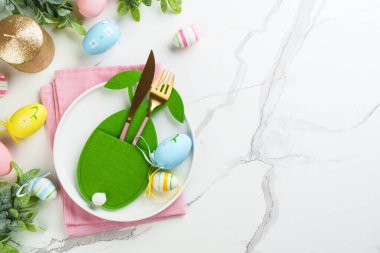 Beyaz arka planda süslemeleri olan Paskalya yemekleri. Beyaz tabak, çatal bıçak takımı ve komik paskalya süslemeleri..