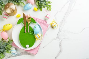 Beyaz arka planda bahar dekorasyonlu Paskalya sofrası. Beyaz tabak, çatal bıçak takımı ve renkli yumurta. Kopyalama alanı olan düz.