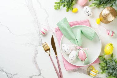Paskalya kompozisyonu. Tatil masası süslemeleri, beyaz tabak, altın çatal bıçak, cam ve renkli paskalya yumurtaları. Üst görünüm.