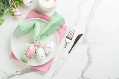 Tatil masası süslemeleri, beyaz tabak, altın çatal bıçak takımı ve renkli paskalya yumurtaları. Kopyalama alanı olan üst görünüm.