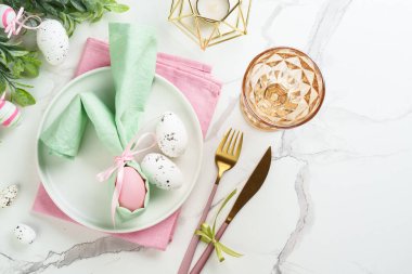 Paskalya kompozisyonu. Tatil masası süslemeleri, beyaz tabak, altın çatal bıçak, cam ve renkli paskalya yumurtaları. Üst görünüm.