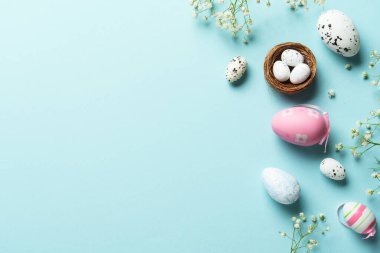 Paskalya yumurtaları, dekorasyonlar ve çiçeklerle sıcak Paskalya kompozisyonu. Üstteki görünüm mavi arkaplan ve kopyalama alanı.
