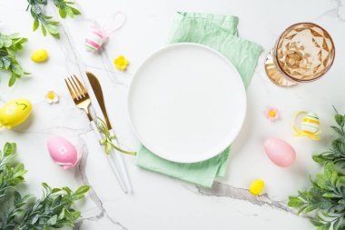 Beyaz arka planda Paskalya sofrası. Beyaz tabak, çatal bıçak takımı ve paskalya süslemeleri. Düz yatıyordu.