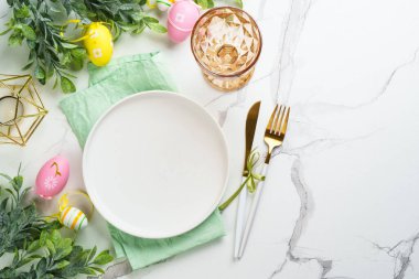 Beyaz arka planda Paskalya yemeği. Beyaz tabak, çatal bıçak takımı, cam ve renkli paskalya süslemeleri. Kopyalama alanı olan düz.