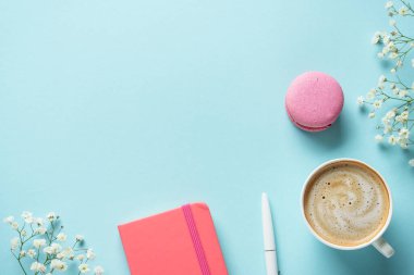 Bir fincan kahve, badem kurabiyesi ve mavi arka planda çiçek. Kopyalama alanı olan üst görünüm.