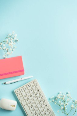 Ofis masasında klavye, defter, kalem ve çiçekler mavi arka planda. Kopyalama alanı olan düz.