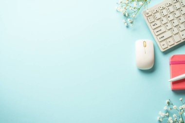 Ofis masasında klavye, defter, kalem ve çiçekler mavi arka planda. Kopyalama alanı olan düz.