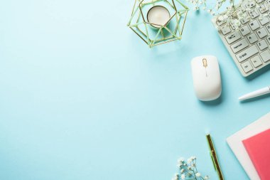 Ofis masasında klavye, defter, kalem ve çiçekler mavi arka planda. Kopyalama alanı olan üst görünüm.