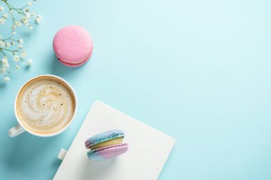 Bir fincan kahve, badem kurabiyesi ve mavi arka planda çiçek. Kopyalama alanı olan üst görünüm.