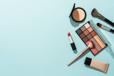 Mavi arka plandaki ürünleri uydur. Kozmetik palet, fırçalar, krem ve ruj. Kopyalama alanı olan düz resim