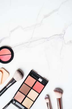 Beyaz mermer arka planda ürünler uydur. Kozmetik palet, fırçalar ve rujlar. Kopyalama alanı olan üst görünüm.