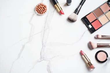Beyaz mermer arka planda ürünler uydur. Kozmetik palet, fırçalar ve rujlar. Kopyalama alanı olan üst görünüm.