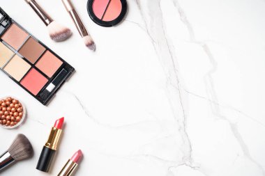 Beyaz mermer arka planda ürünler uydur. Kozmetik palet, fırçalar ve rujlar. Kopyalama alanı olan üst görünüm.