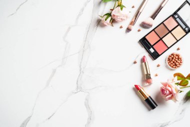 Beyaz mermer arka planda çiçekli ürünler uydur. Kozmetik palet, fırçalar ve rujlar. Kopyalama alanı olan üst görünüm.