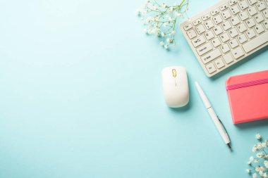 Ofis masasında klavye, defter, kalem ve çiçekler mavi arka planda. Kopyalama alanı olan düz.