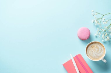 Bir fincan kahve, badem kurabiyesi ve mavi arka planda çiçek. Kopyalama alanı olan üst görünüm.