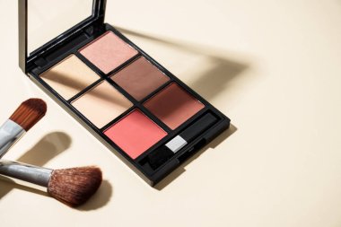 Pastel arka planda sert gölgeli palet ve kozmetik fırçalar yap.