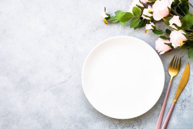 Masa seti beyaz tabak, çatal bıçak takımı ve gül çiçekli şarap kadehi. Yıldönümü ya da düğün için masa dekorasyonu. Kopyalama alanı olan düz.