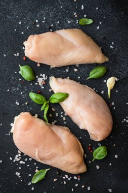 Tavuk fileto, çiğ tavuk göğsü, baharat ve siyah arka planda bitkiler. Metin için boşluk olan üst görünüm.