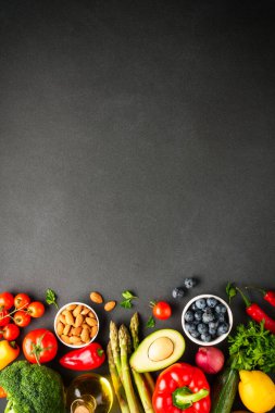 Siyah arka planda sağlıklı yiyecekler. Taze sebze, yapraklar ve fındık. Dikey resim.