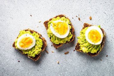Open sandwich. Whole grain bread with avocado and boiled eggs. Top view on stone background.