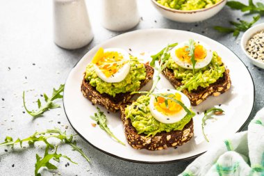 Avocado sandwich. Whole grain bread with avocado and boiled eggs with arugula. Top view on white background.