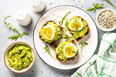 Open sandwich. Whole grain bread with avocado and boiled eggs. Top view on white kitchen table.