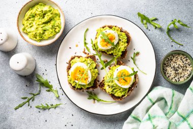 Open sandwich. Whole grain bread with avocado and boiled eggs. Top view on white kitchen table.