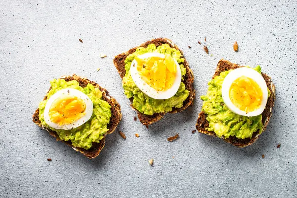 Open sandwich. Whole grain bread with avocado and boiled eggs. Top view on stone background.