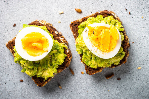 Open sandwich with avocado and boiled eggs. Top view on stone background.
