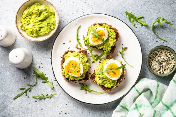 Open sandwich. Whole grain bread with avocado and boiled eggs. Top view on white kitchen table.
