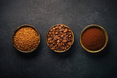 Roasted coffee beans, ground coffee and instant coffee in bowls at dark background. Top view image.