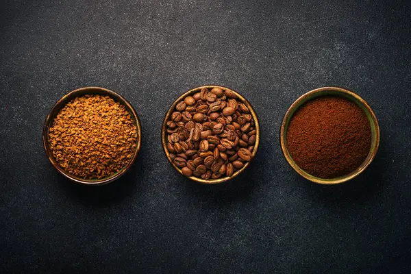 Roasted coffee beans, ground coffee and instant coffee in bowls at dark background. Top view image.