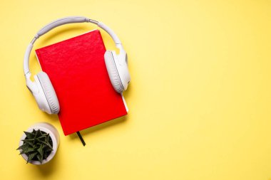 Audio book concept. Headphones, book and green plant at yellow background. Flat lay image with copy space.